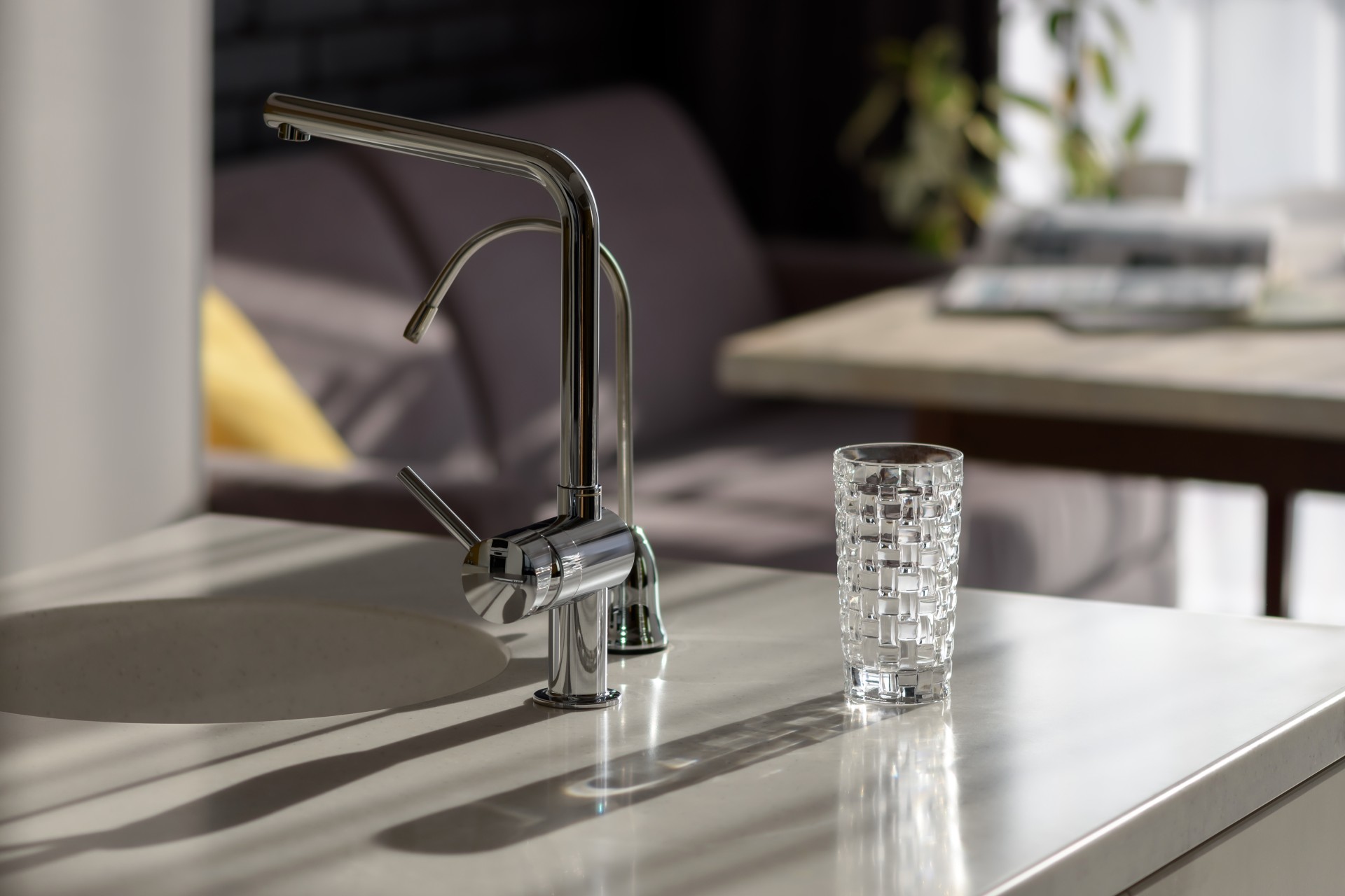 Glass of pure filtered water on the kitchen table in the rays of sunlight. Kitchen faucet and reverse osmosis faucet for water p